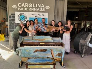 People lifting one person behind a painted piano