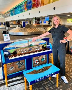 Artist stands next to piano she painted in an airplane theme