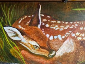 Close-up of fawn resting in grass on a painted piano