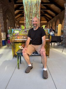 Artist sitting at nature-themed painted piano