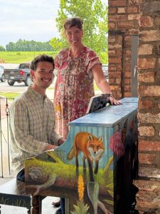 Two people pose near painted piano