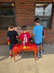 Three boys play a painted piano