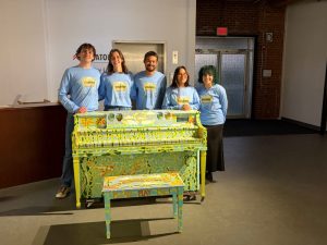 Artists stand behind painted piano